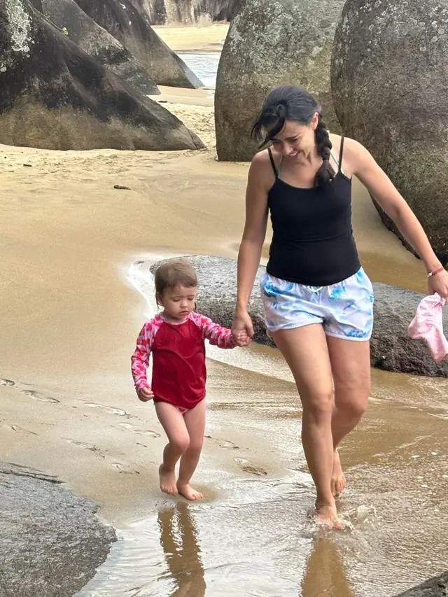 Aline Favaro andando na praia com a filha